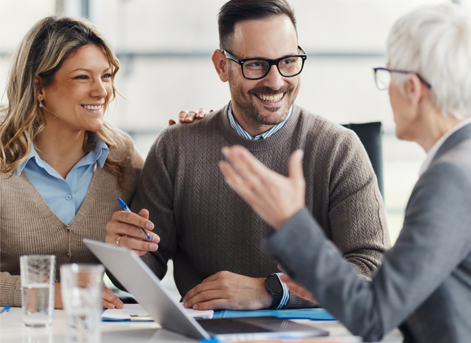 Lächelndes Paar bei Beratungsgespräch mit einer Beraterin, Fokus auf Vertrauen und Zusammenarbeit.